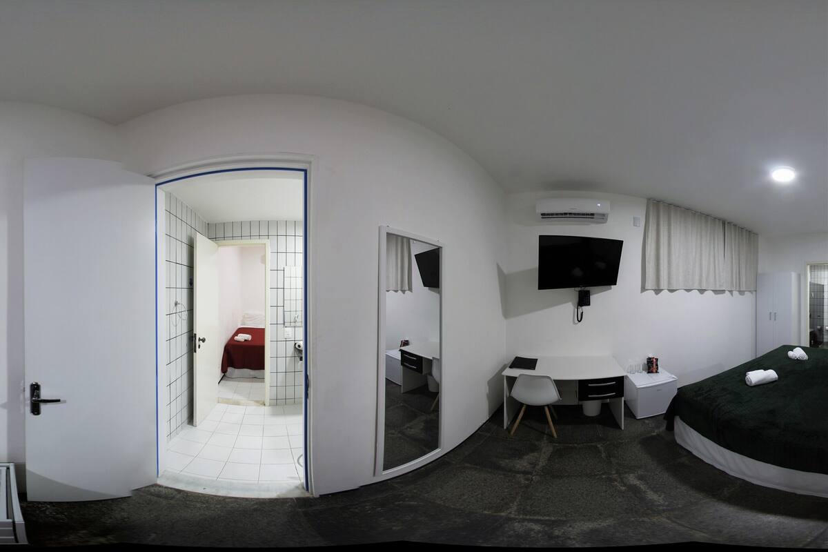 A modern hotel room with a curved layout, a desk, a TV, and a bed.