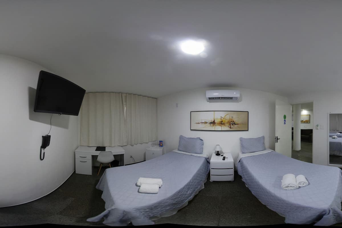 A hotel room with two beds, a desk, a chair, a TV, and a painting on the wall.