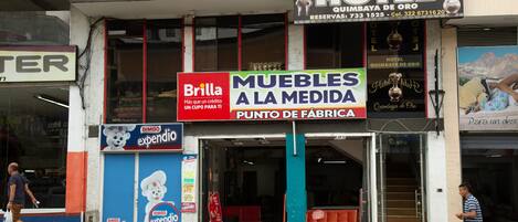 A hotel with a sign for 'Hotel Quimbaya de Oro' and a furniture store named 'Brilla' with a sign 'MUEBLES A LA MEDIDA'.
