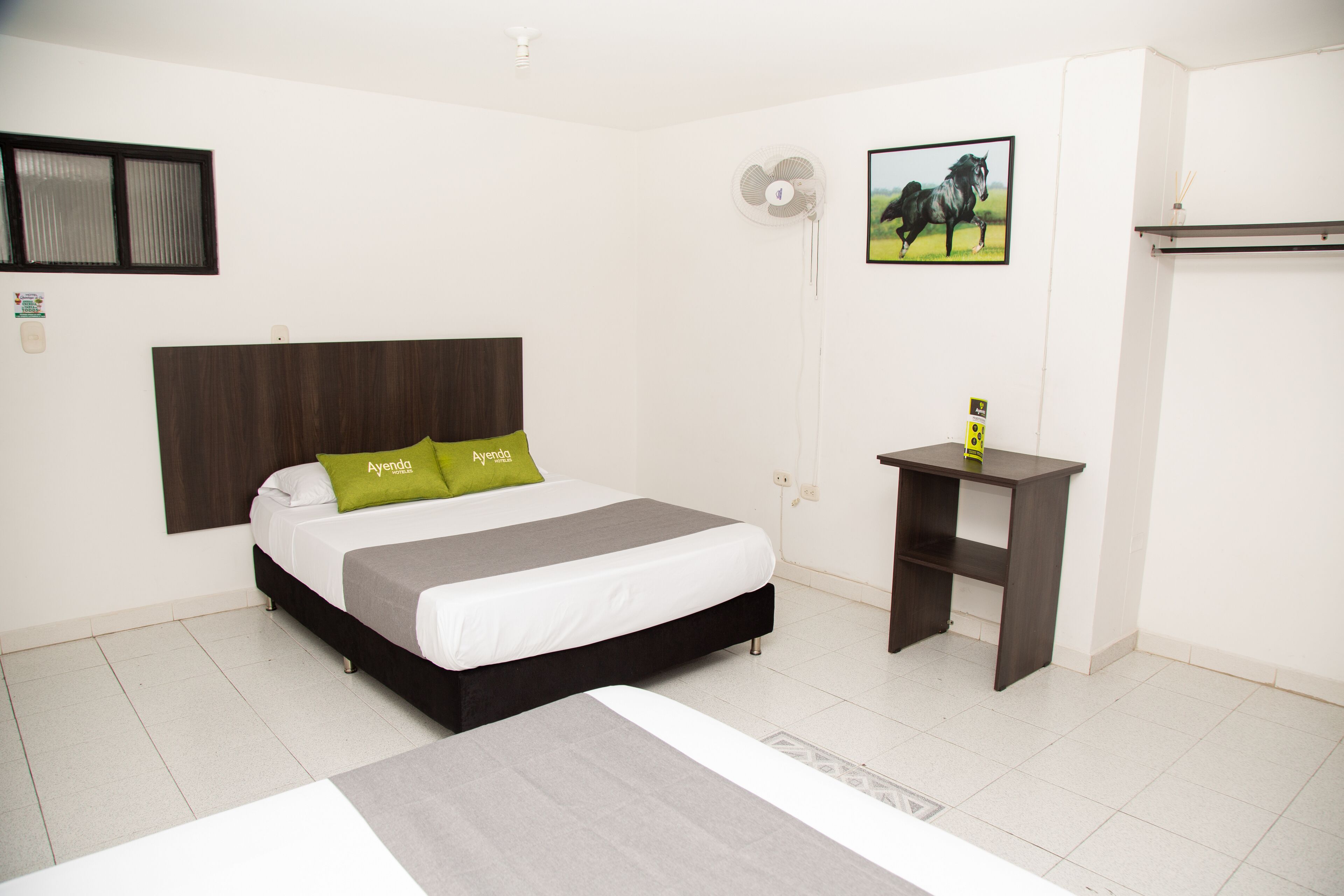 A bedroom with a bed, a bedside table, a fan, and a picture on the wall.
