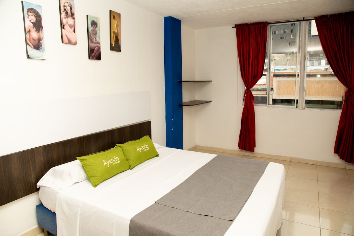 Ein Hotelzimmer mit Bett, Fenster mit roten Vorhängen und einem Bild an der Wand.