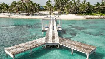 A wooden pier extending into turquoise waters, surrounded by palm trees and a sandy beach.