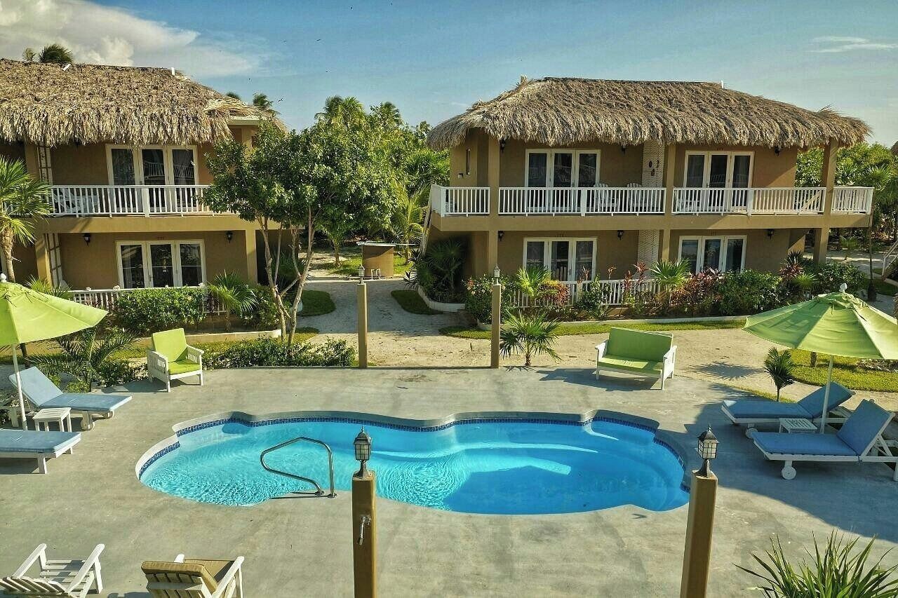 A resort with two thatched-roof buildings, a central swimming pool, and lounge chairs.