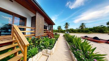 A modern building with a wooden staircase leading to a covered porch, a sandy pathway, and a red kayak on the beach.