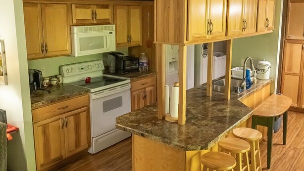 Una cocina con armarios de madera, microondas, estufa y una barra con taburetes.