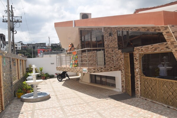 A courtyard with a fountain, potted plants, a motorcycle, and a building with a balcony.