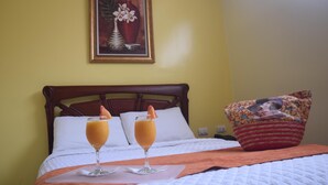 A hotel room with a bed, two drinks on a tray, a painting on the wall, and a pillow with a floral pattern.