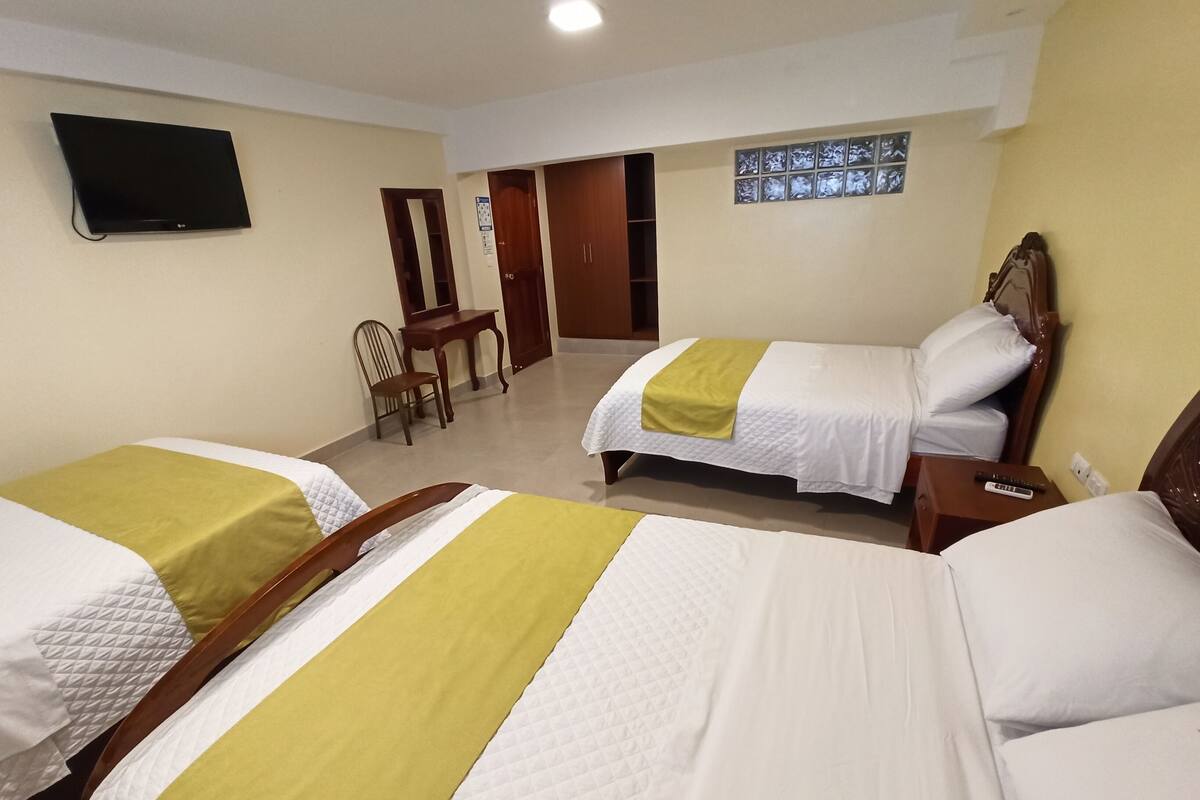 A hotel room with two beds, a TV mounted on the wall, and a small desk with a chair.