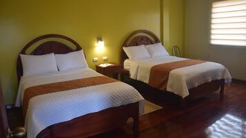 A room with two wooden beds, each with a headboard, a bedside table, and a lamp.