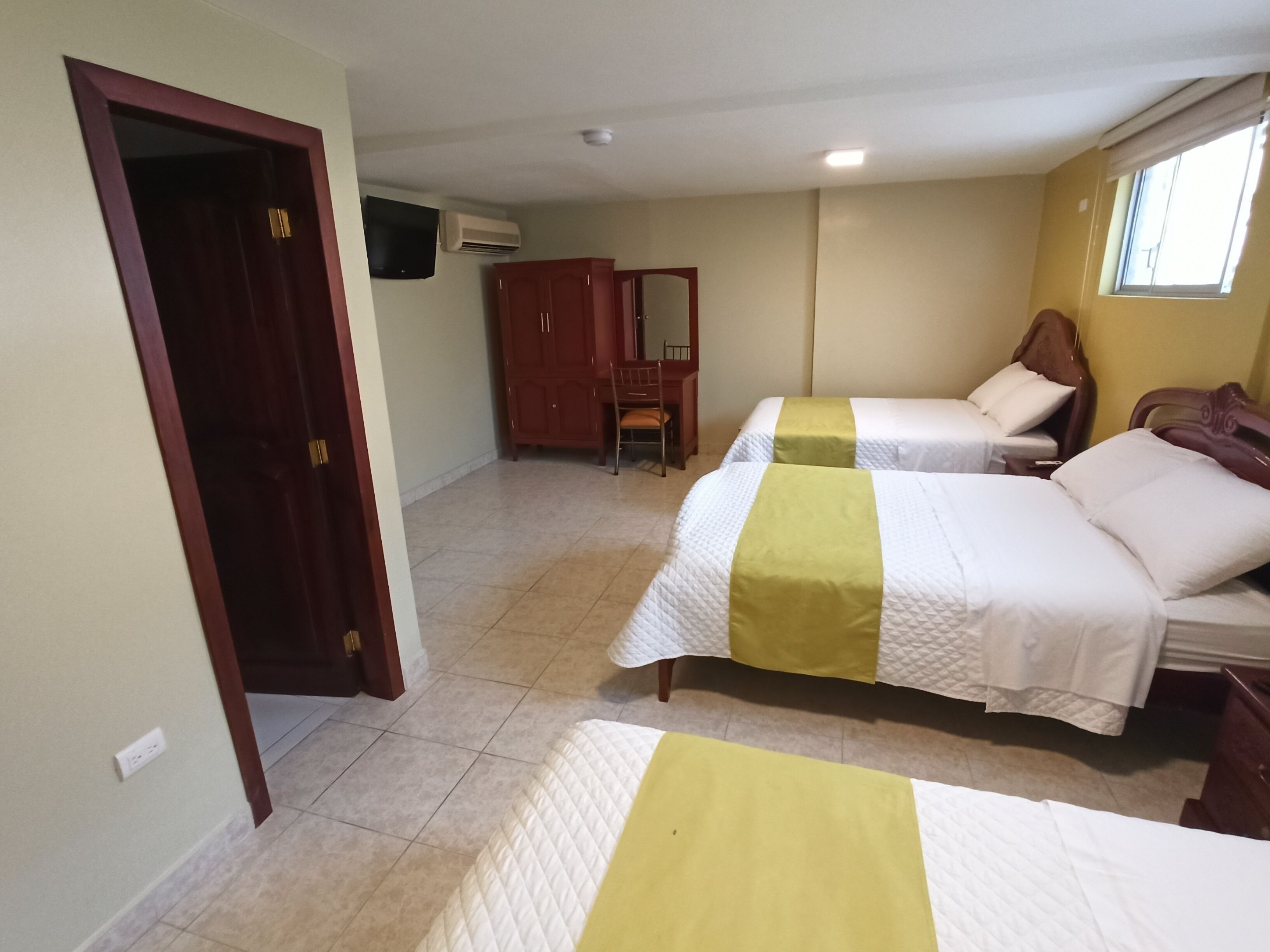 A hotel room with two beds, a wooden wardrobe, a desk, and a chair.