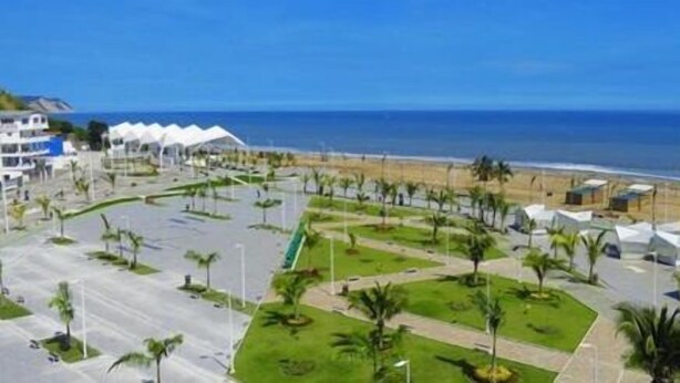 A coastal hotel with a beach view, featuring a parking lot, green spaces, and white buildings.