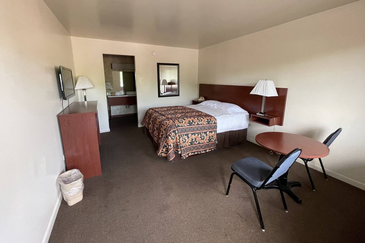 A hotel room with a bed, bedside table, chair, desk, and a small table with a lamp.