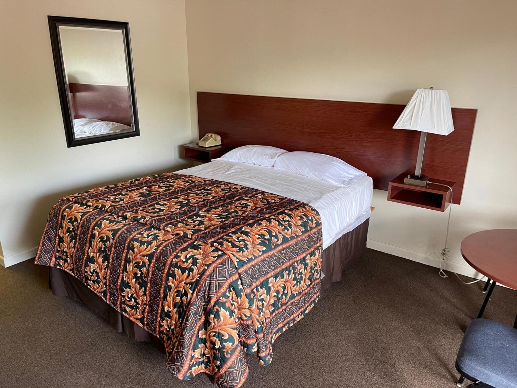 A hotel room with a bed, a nightstand with a lamp, a chair, and a small table.