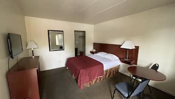 A hotel room with a bed, a desk, a chair, a TV, and a mirror.