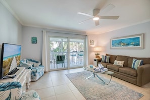 A living room with a sofa, a coffee table, a TV, and a balcony with chairs.