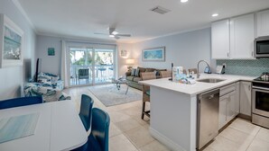 A modern kitchen with white cabinets, a central island, and a dining area with blue chairs. - Island Retreat by SeaBreeze Vacation (Holmes Beach)