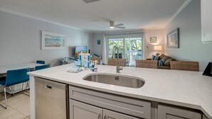 A modern kitchen with a central island, a dining area with blue chairs, and a cozy seating area with a sofa and cushions. - Island Retreat by SeaBreeze Vacation (Holmes Beach)