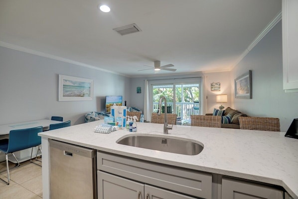 A kitchen with a central island, a dining area with blue chairs, and a seating area with a sofa and cushions.