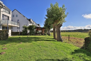 A residential area with modern buildings, a grassy lawn, and a large tree. - Haffblick Whg. Ha03, Deutschland (Ostseebad Boltenhagen)