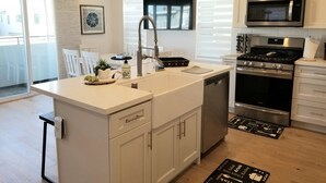A modern kitchen with a central island, stainless steel appliances, and a dining area with a view. - The ultimate beach getaway charming 3-bdrm 2-bath home steps from a sandy Beach (Oxnard)