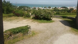 Une vue sur la côte, avec un sentier de terre, de la végétation et des maisons au loin.