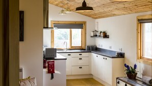 A compact kitchen with wooden ceiling beams, a window with a view, and a fire blanket on the wall.
