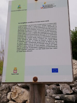 A sign with text about coral reefs and green rocks, featuring logos of Regione Puglia and the European Union.