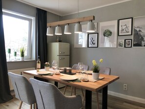 Un comedor con una mesa de madera, sillas grises y un refrigerador de color claro al fondo.