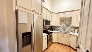 A compact kitchen with white cabinets, a stainless steel refrigerator, a microwave, and a stove. - RedCliff Haven - Pool - HotTub - Aug availability (Moab)