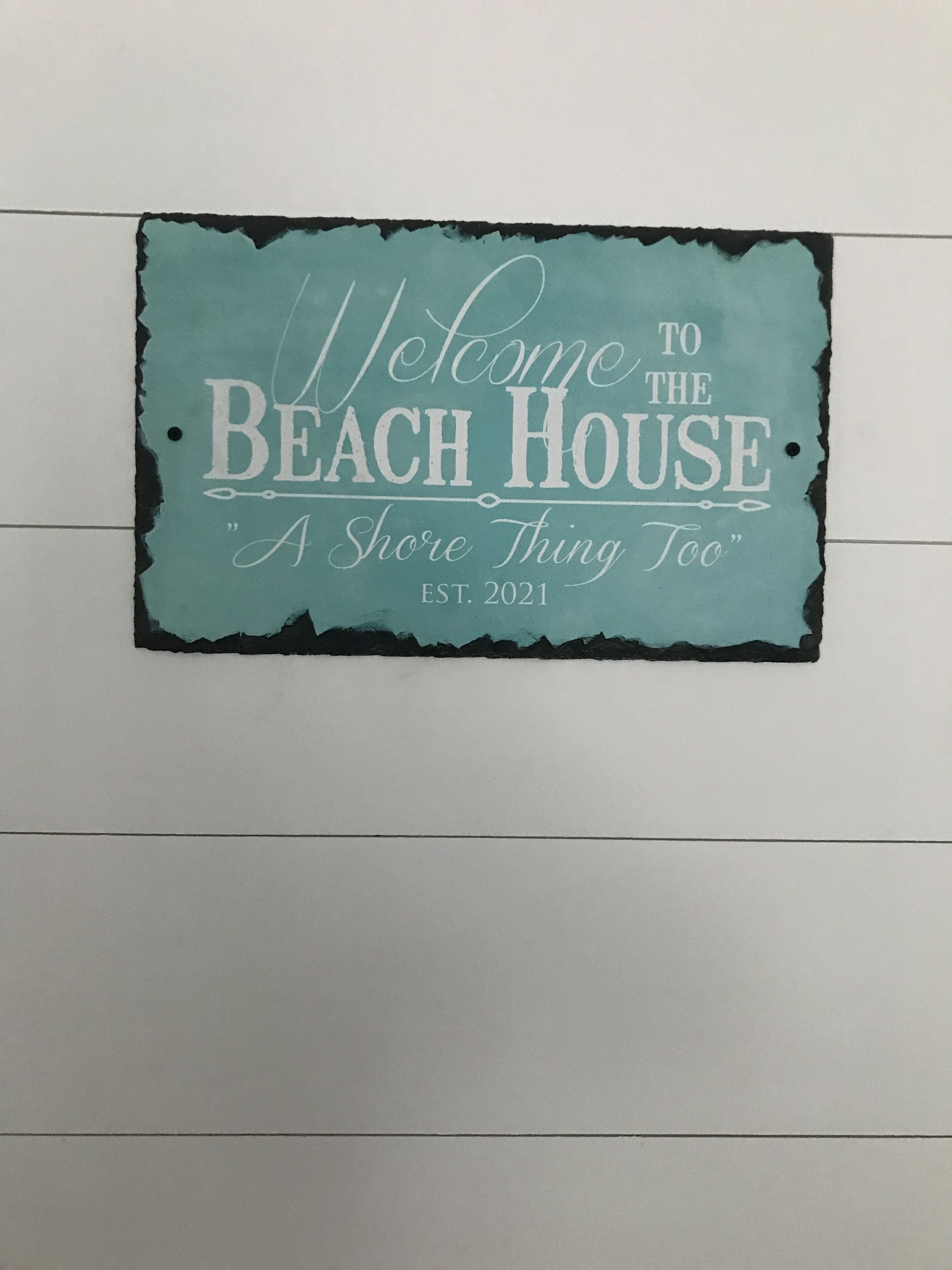 A sign with the text "Welcome to the Beach House A Shore Thing Too" and "EST. 2021".