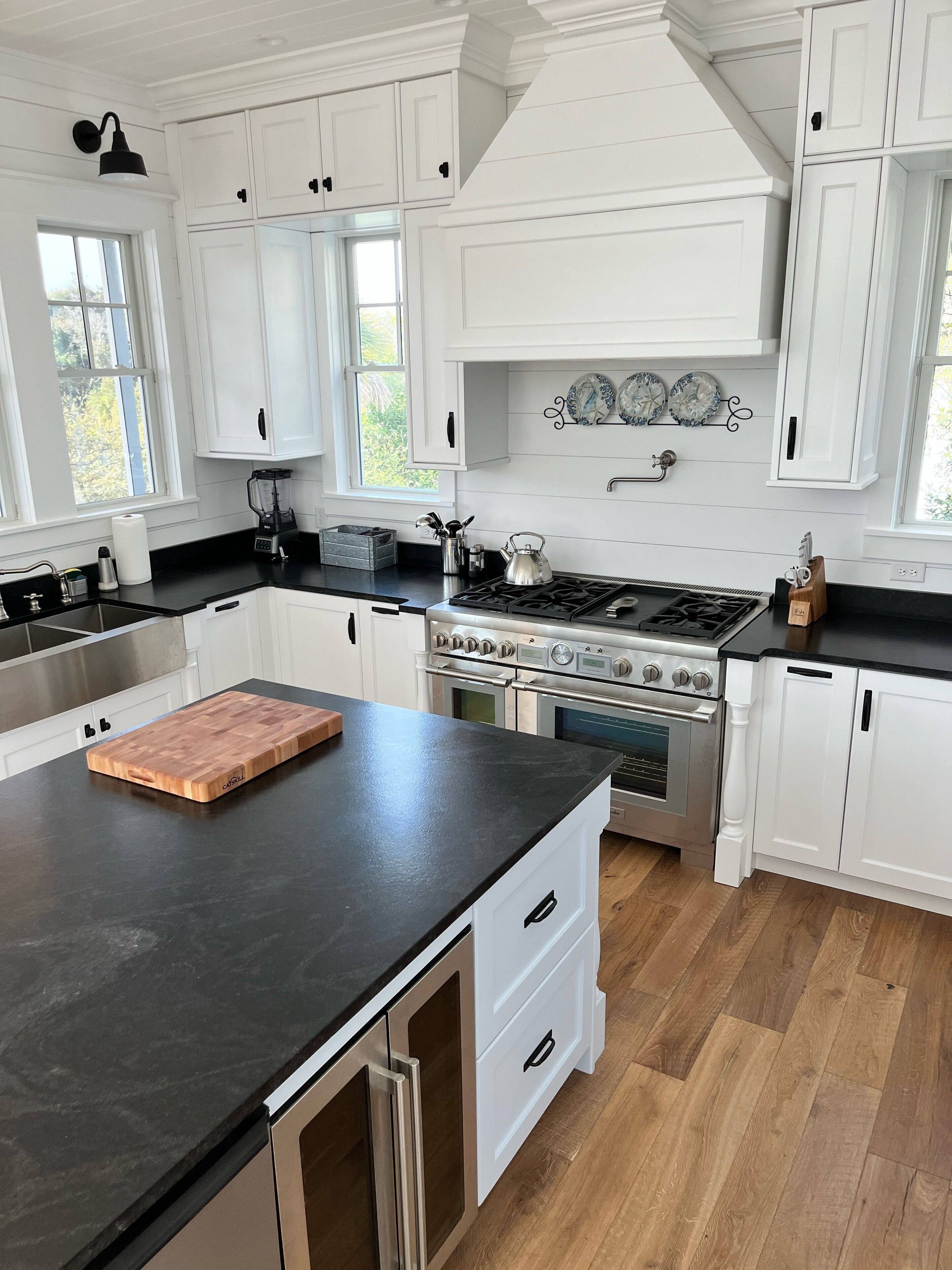 A modern kitchen with white cabinetry, a large island with a cutting board, stainless steel appliances, and a window providing natural light.