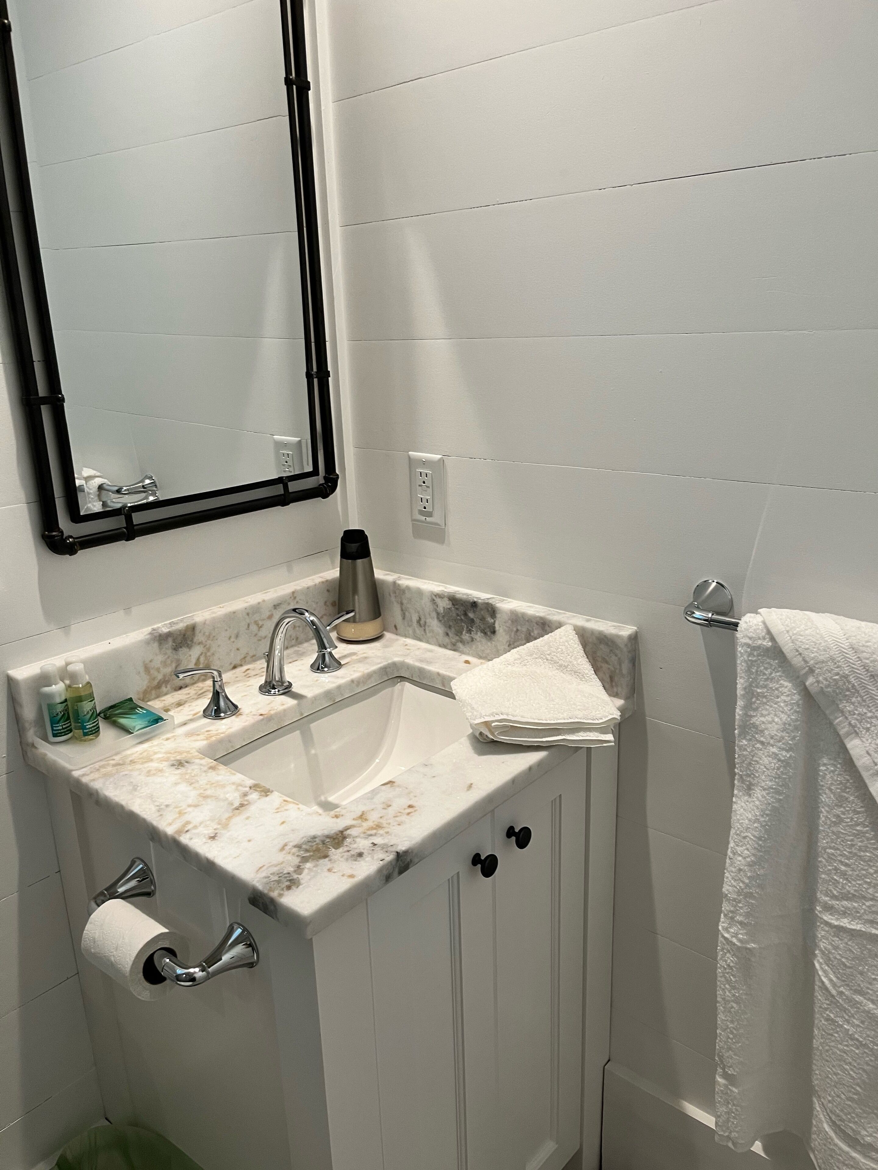 A bathroom with a white sink, two faucets, a mirror, a towel rack, and a toilet paper holder.