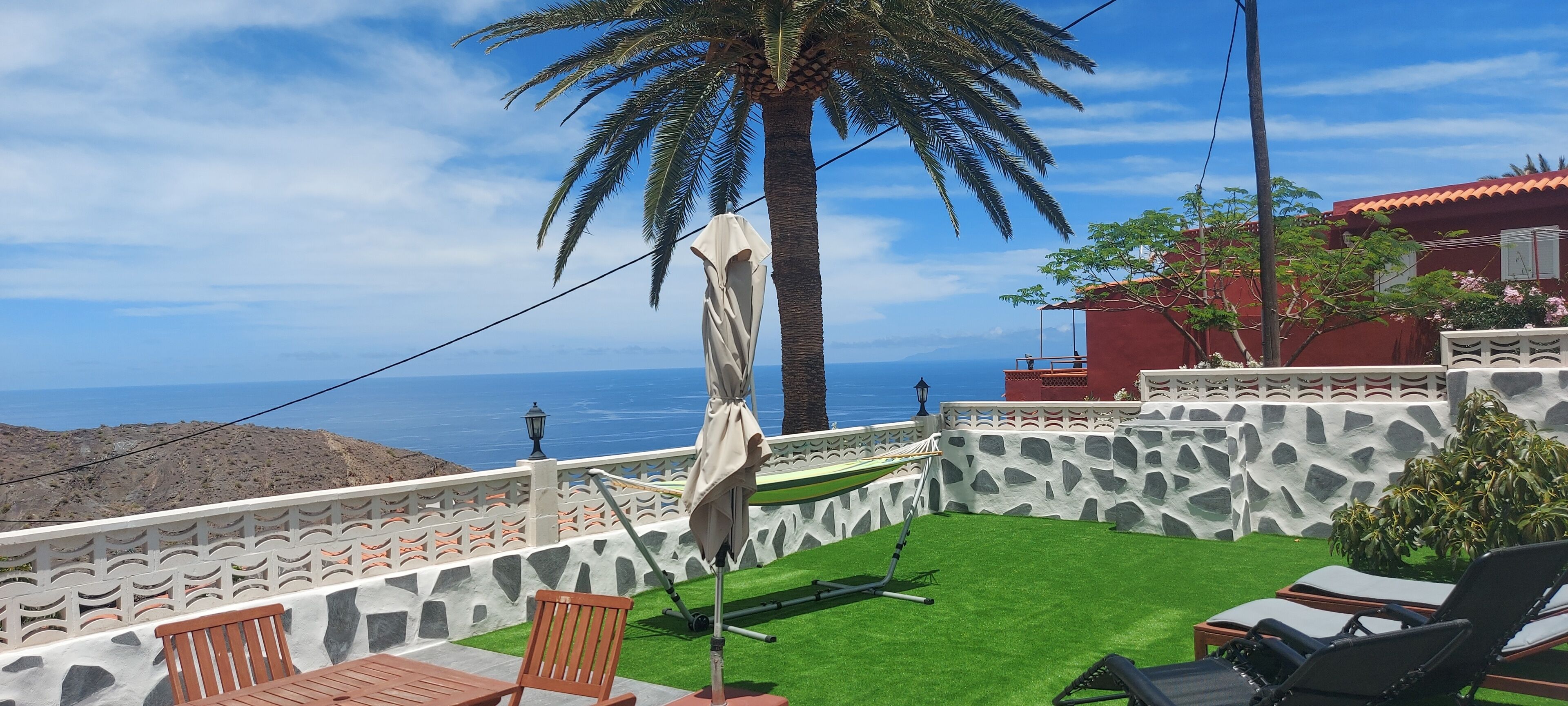 Eine Terrasse mit einer Hängematte, einem Tisch und Stühlen mit Blick auf eine felsige Landschaft und das Meer.