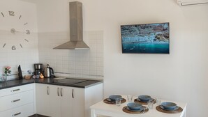 Moderni keittiö, jossa on valkoiset kaapit, ruostumattomasta teräksestä valmistettu liesituuletin sekä ruokapöytä, jonka päällä on sinisiä kulhoja ja lautasia.