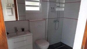 Ein kleines Badezimmer mit einem weißen Waschbecken, einer Toilette und einer Duschkabine.