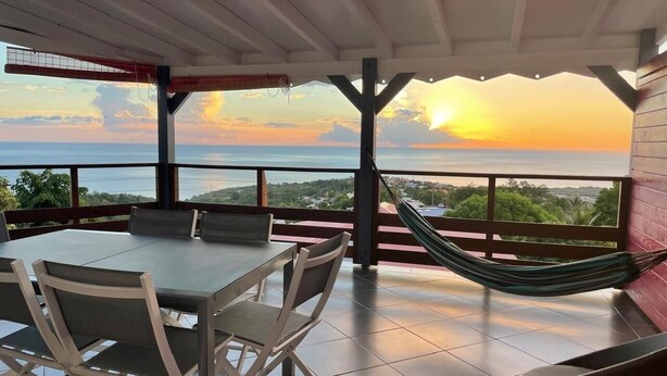 Eine Terrasse im Freien mit Tisch und Stühlen, einer Hängematte und Blick auf den Sonnenuntergang über dem Meer.
