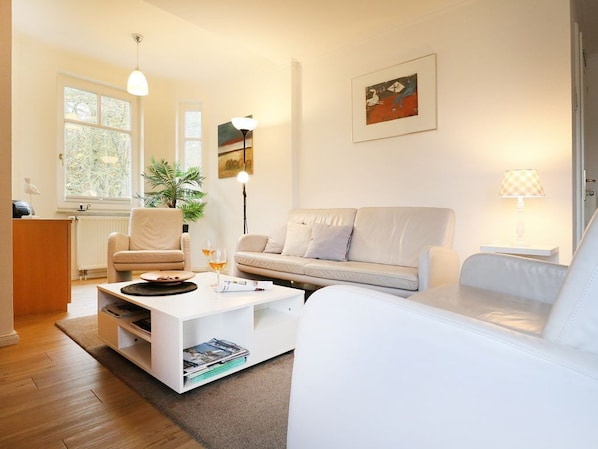 A modern living room with a white sofa, a white coffee table, a floor lamp, and a painting on the wall. - Deutsches Haus Whg. DH8 (Ostseebad Boltenhagen)