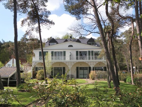 Un bâtiment à deux étages doté d’un balcon, entouré d’arbres et d’une pelouse bien entretenue.