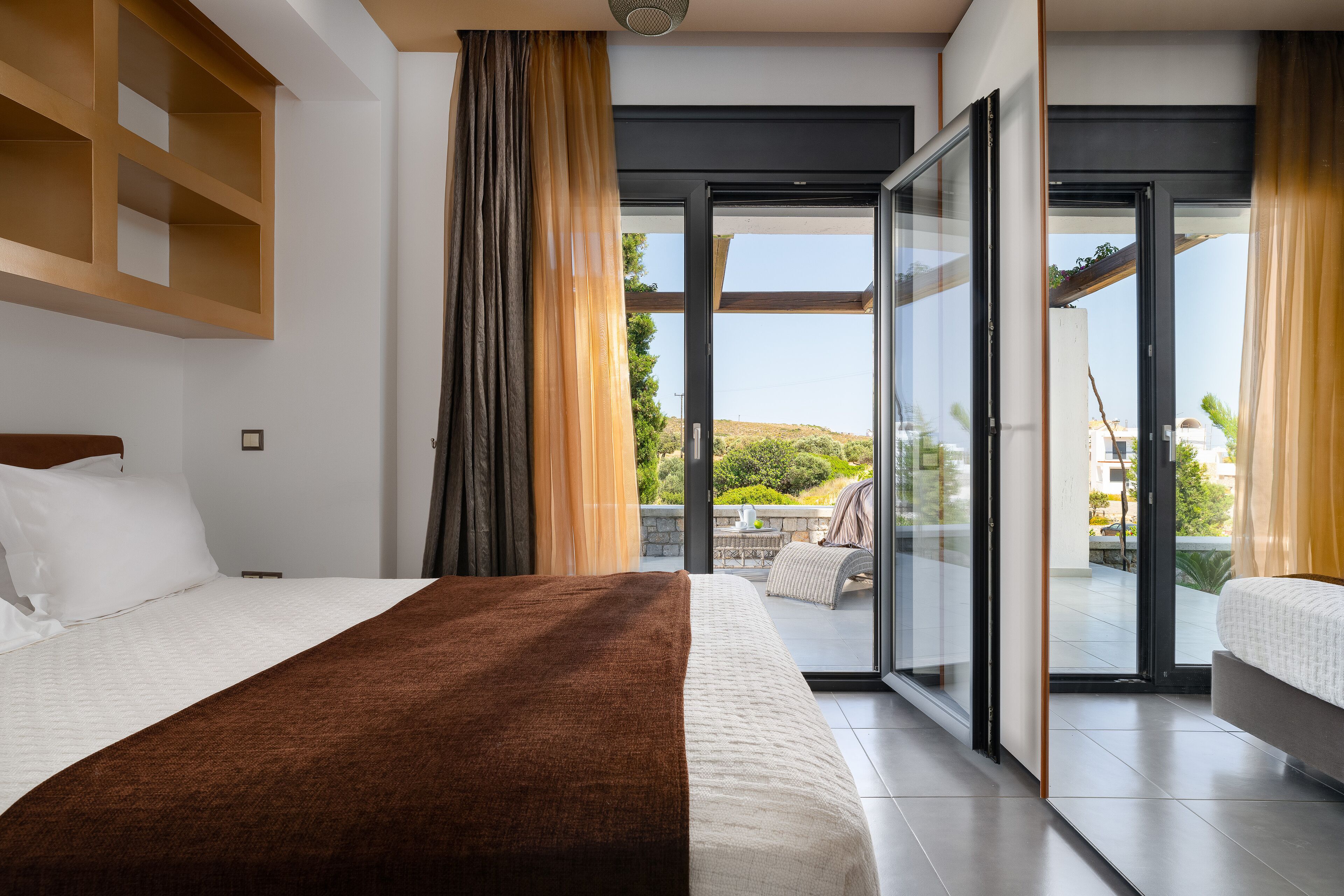 Una habitación de hotel moderna con una cama grande, un balcón con vistas al paisaje y un ventanal corredero.