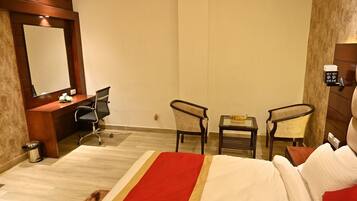 A hotel room with a bed, a desk, two chairs, a small table, a trash bin, and a wall-mounted coffee machine.