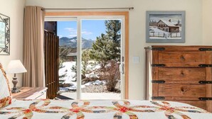 A bedroom with a large bed, a wooden dresser, a painting, and a sliding glass door leading to a snowy outdoor area. - Longs Peak Lodge; An Easy walk to downtown! #3221 (Estes Park)
