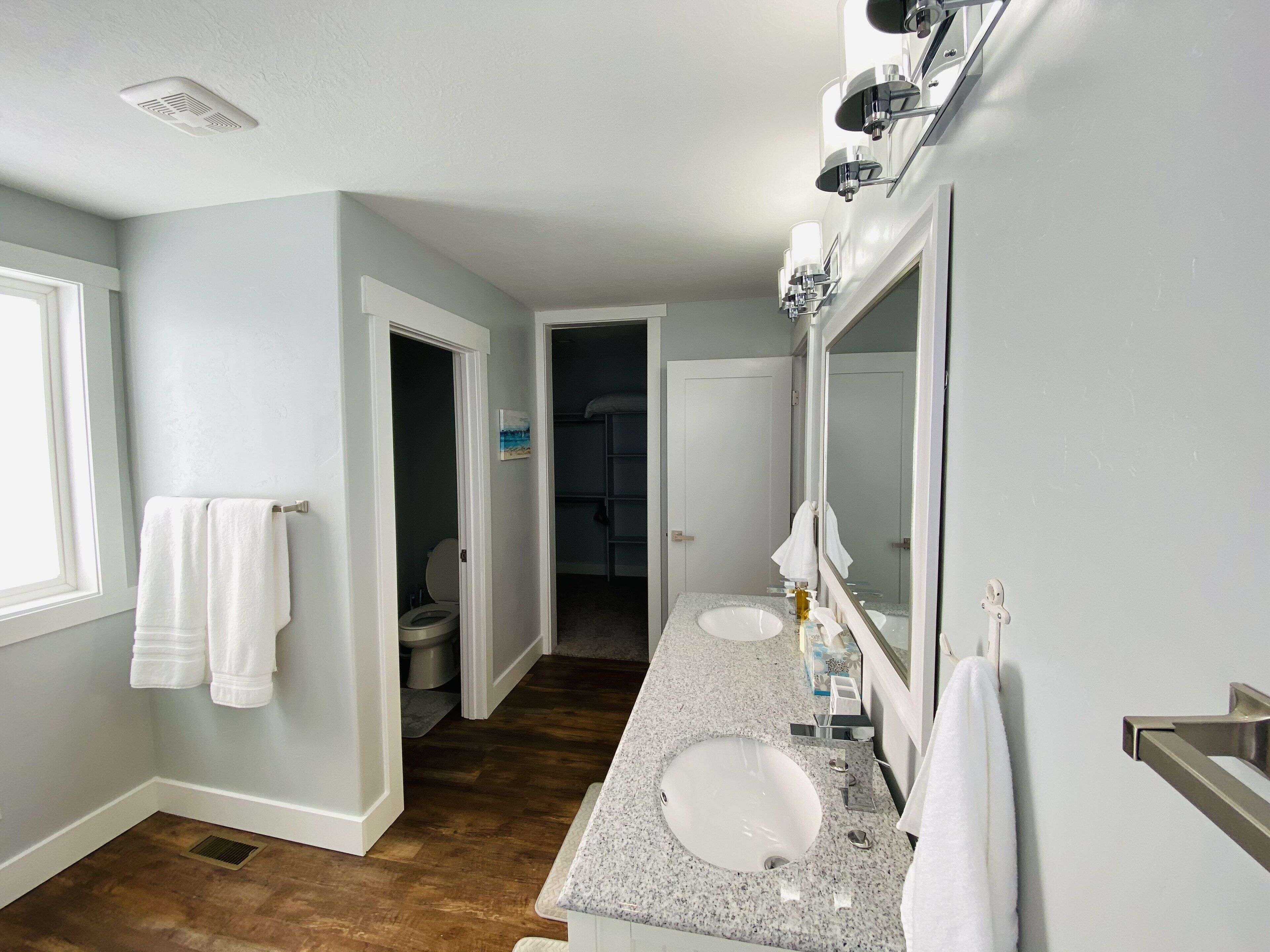 A modern bathroom with two sinks, a large mirror, and a walk-in closet.