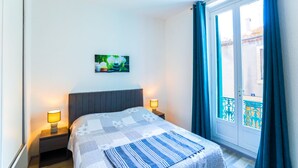A bedroom with a bed, two bedside lamps, a wall-mounted painting, and a balcony with blue curtains. - Apartment Les Halles: 80 m2, terrace 30 m2 air conditioning, garage, 8 beds (Narbonne)