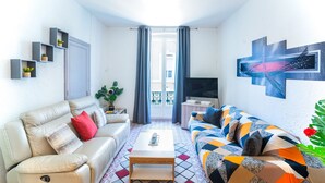 A modern living room with a beige sofa, a colorful patterned sofa, a coffee table, a TV, and a balcony with curtains. - Apartment Les Halles: 80 m2, terrace 30 m2 air conditioning, garage, 8 beds (Narbonne)