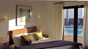 Habitación de hotel con cama, dos lámparas de noche, un cuadro en la pared y vistas a una piscina a través de una puerta corrediza de cristal.