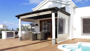 Un patio techado al aire libre con una parrilla, comedor y piscina.