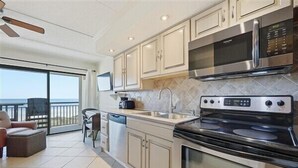 Una cocina moderna con una estufa grande, microondas y lavavajillas. Hay una puerta corrediza de vidrio que da a un balcón con vistas.