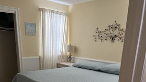 Une chambre à coucher avec un lit, une table de chevet, une lampe, un élément de décoration murale et une porte.