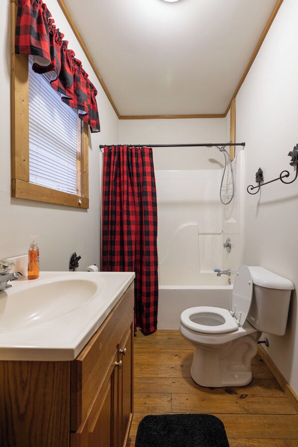 Ein Badezimmer mit einem Holzbadezimmermöbel, einem weißen Waschbecken, einer Toilette und einer Dusche mit einem rot-schwarz karierten Vorhang.
