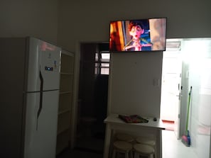 Una cocina pequeña con un refrigerador, un televisor sobre una encimera y una puerta que da a otra habitación.